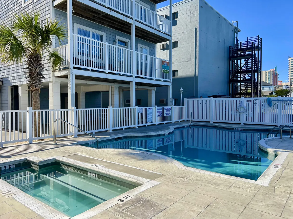 The image features a sparkling swimming pool surrounded by palm trees, balconies, and sun loungers. The relaxed atmosphere invites guests to take a dip or lounge with family after a morning at the beach.