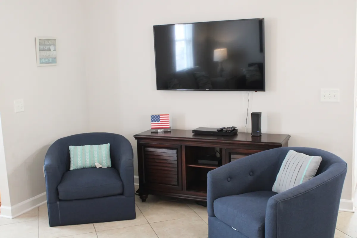 This scene features two blue accent chairs facing a flat-screen TV on a wooden stand, creating a welcoming entertainment zone within the living space. The mood is comfortable and relaxed, ideal for movie nights or watching the big game.