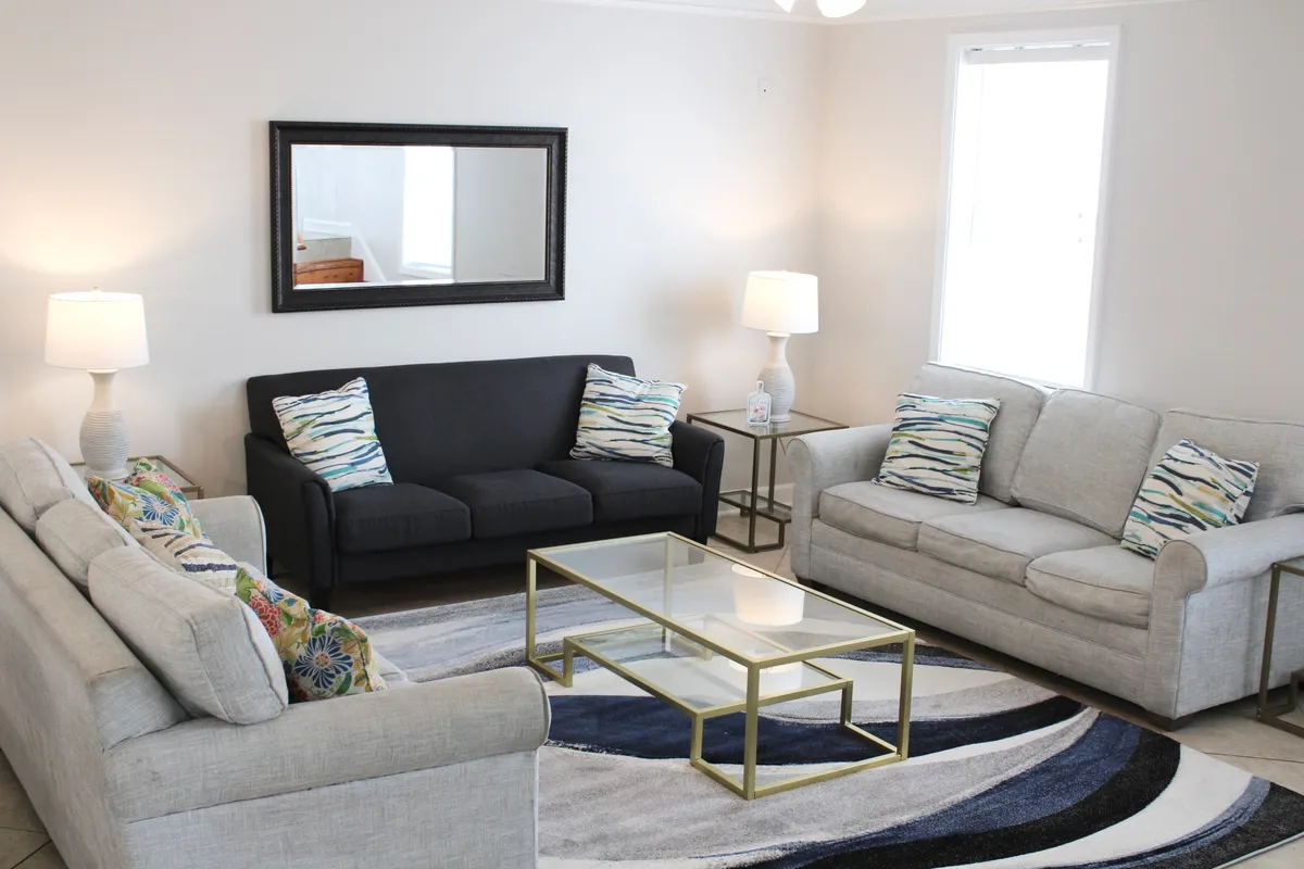 This image showcases a comfortable, open living room with plush sofas, a coffee table, decorative pillows, a stylish rug, and a wall mirror. The seating arrangement is inviting, encouraging guests to relax and engage in conversation or activities.