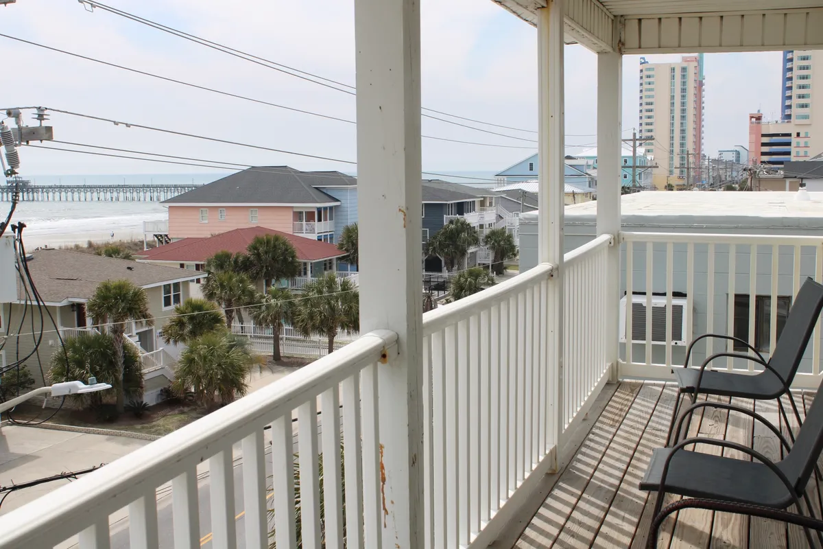 This image showcases a tranquil balcony overlooking Cherry Grove Beach, with a clear view of the sandy shoreline, gentle waves, and nearby beach houses. The inviting balcony rail provides a perfect vantage point for soaking in the sights and sounds of the ocean.