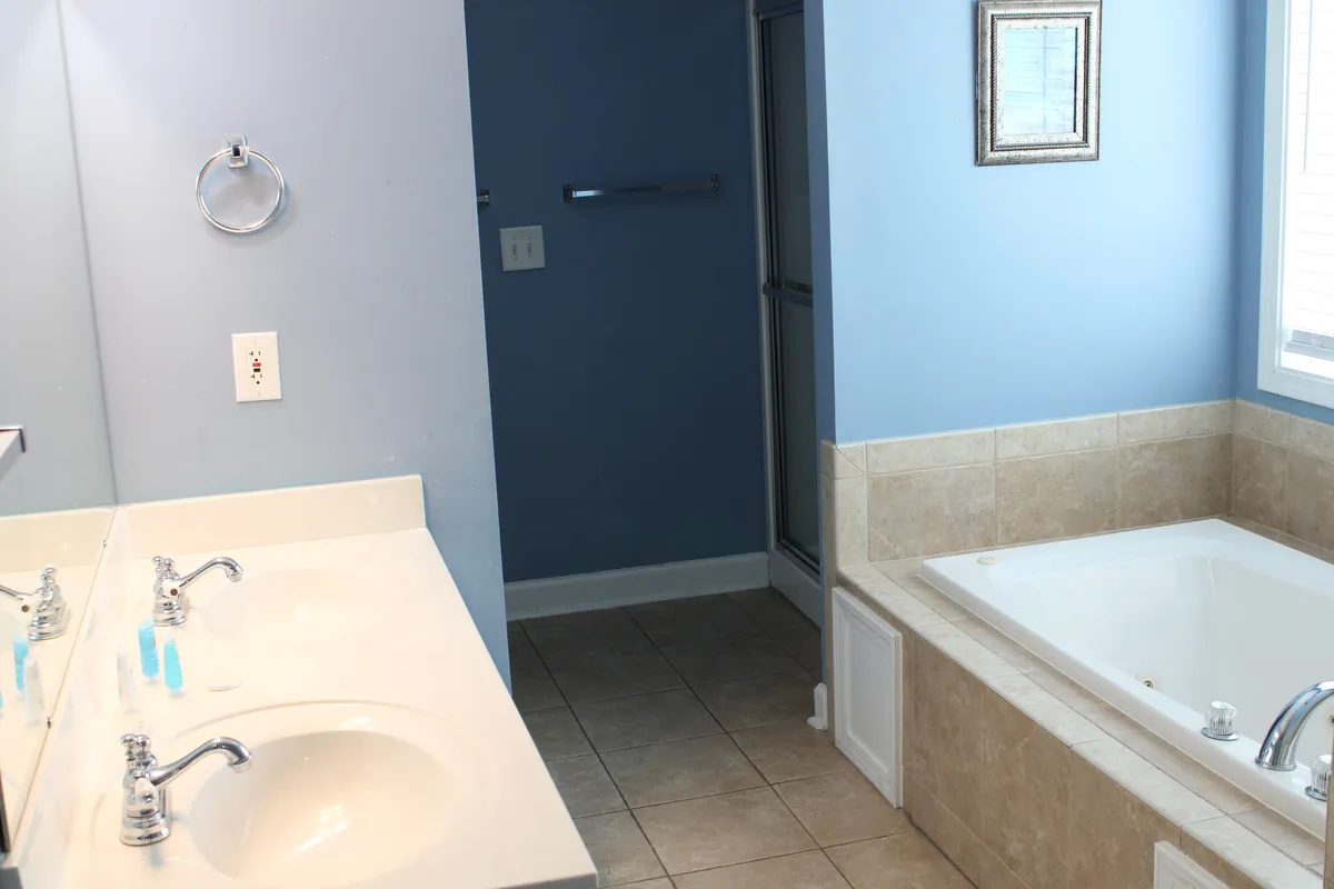 A modern, spacious bathroom with double vanity sinks, a large bathtub, a separate shower area, and decorative framing on the wall. The space is bright and inviting, perfect for both self-care and privacy.