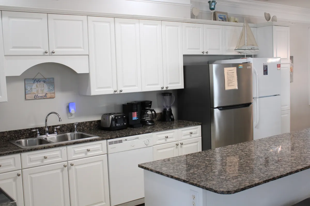 This image showcases a spacious, modern kitchen featuring granite countertops, sleek white cabinetry, and premium kitchen appliances. The scene captures a welcoming, lively atmosphere where people are gathered, cooking, and socializing, with an inviting sense of connection and activity.