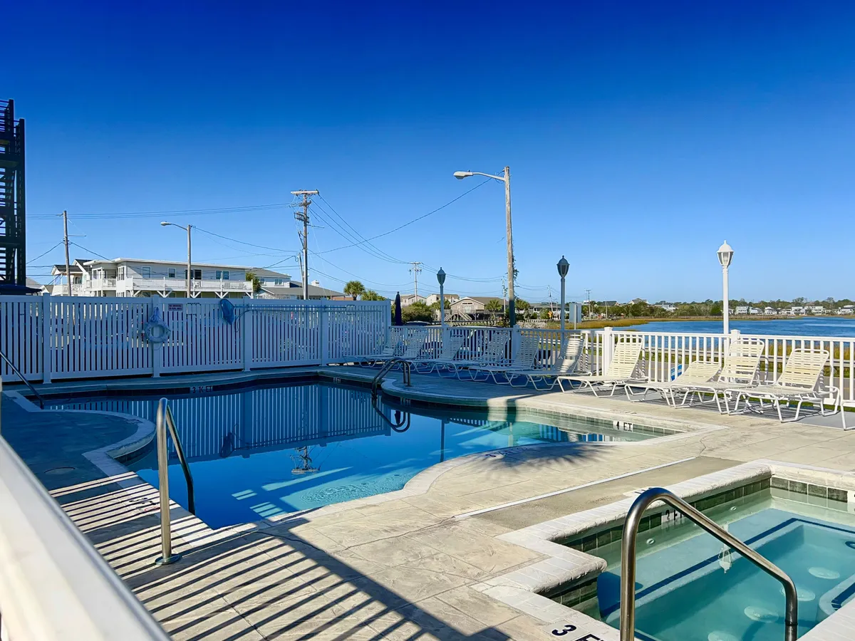 This exterior image captures a sparkling swimming pool and hot tub surrounded by inviting lounge chairs, all enclosed within a secure fence. The layout suggests a perfect communal area for group activities such as poolside barbecues, sunbathing, and relaxed social gatherings. The tranquil setting hints at opportunities for both lively group fun and comfortable downtime.